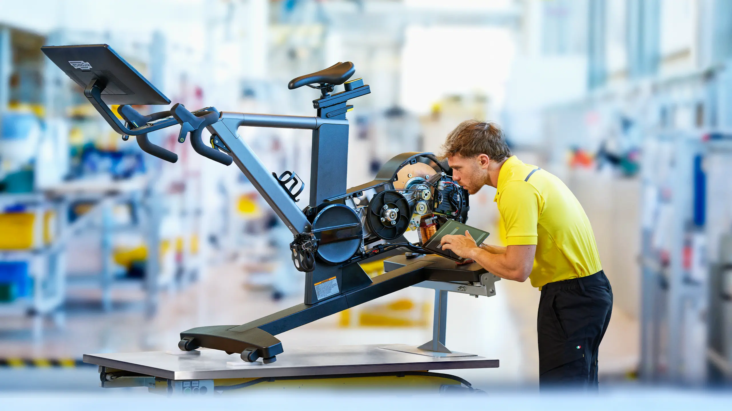 Technician inspecting and refurbishing a used Technogym Ride exercise bike inside the professional workshop environment of the Technogym Village