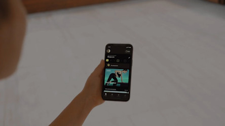 Egy személy okostelefont tart a kezében, amelyen a Technogym alkalmazás látható, és egy videó látható valakiről, aki jógázik.
