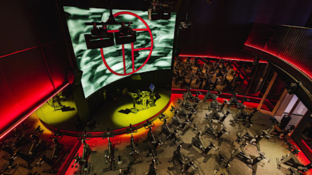 Beltéri kerékpáros stúdió a Totalfusion Morningside-ban. Sorokban elhelyezett Group Cycle Connect kerékpárok, halvány piros és sárga világítás, nagyméretű képernyő a Totalfusion logójával. Emelt platform az oktatókerékpárnak.