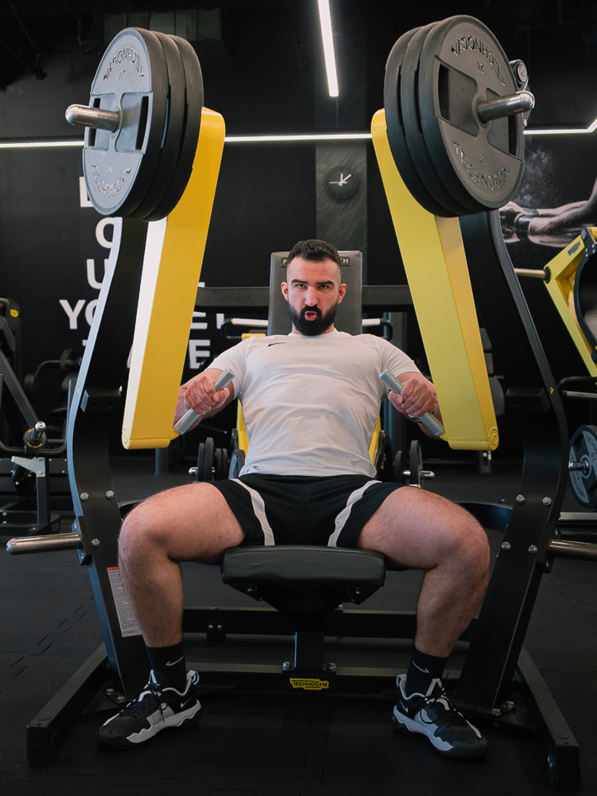 A dark-haired, muscled bodybuilder training on a Technogym Chest Press machine