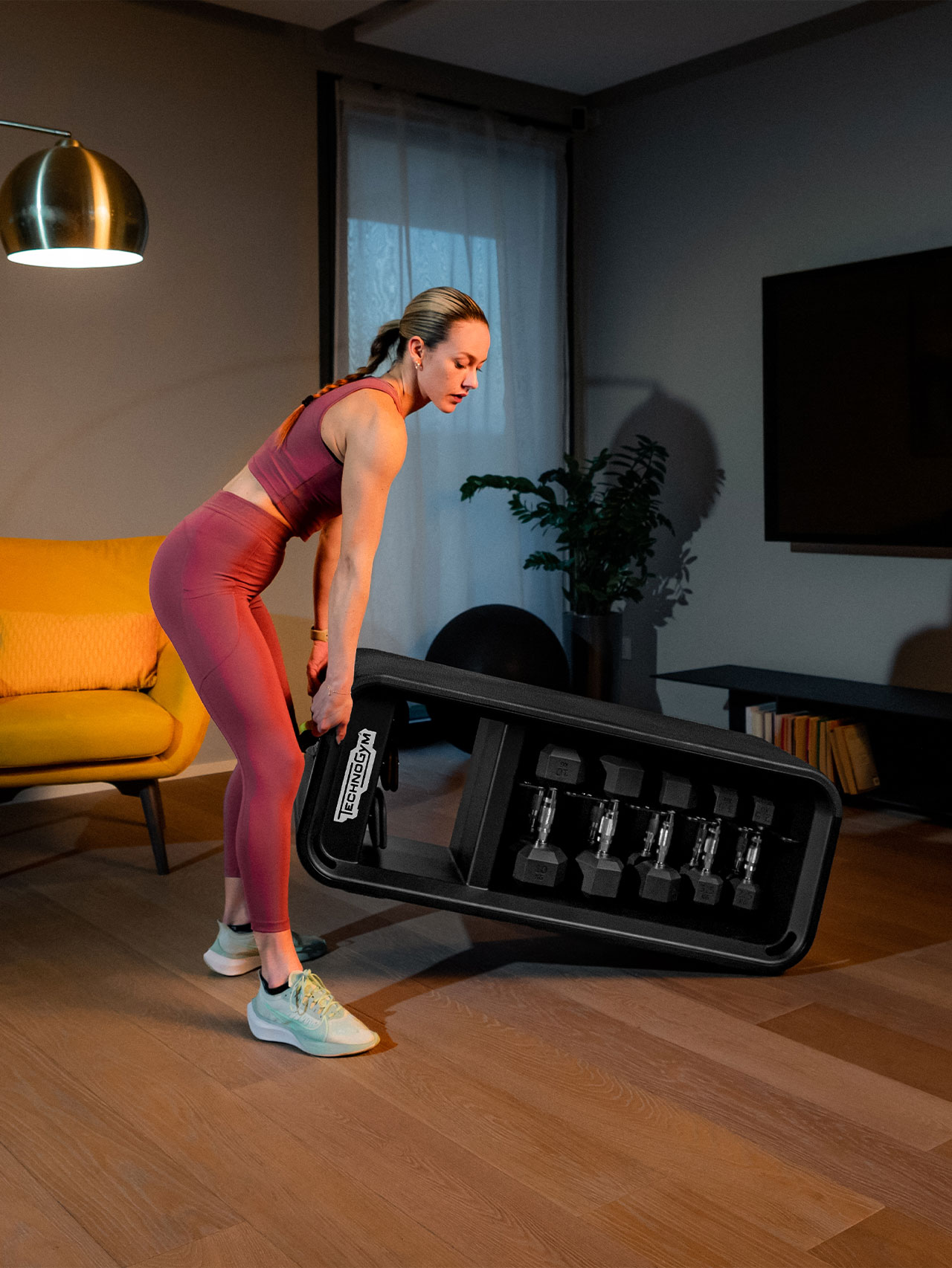 Young lady lifting the Technogym Bench multi functional bench with weights to move it to another location by rolling it on the two front wheels