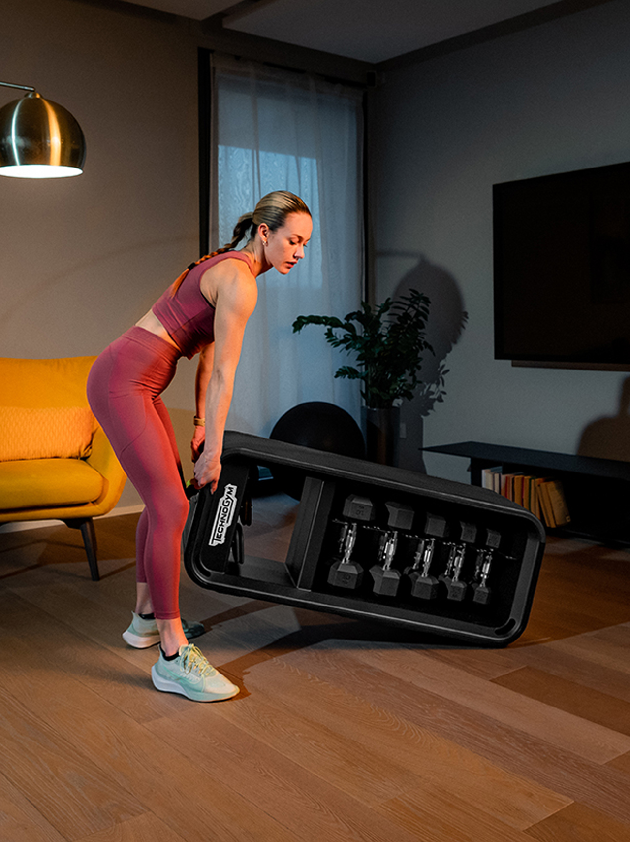 Young lady lifting the Technogym Bench multi functional bench with weights to move it to another location by rolling it on the two front wheels