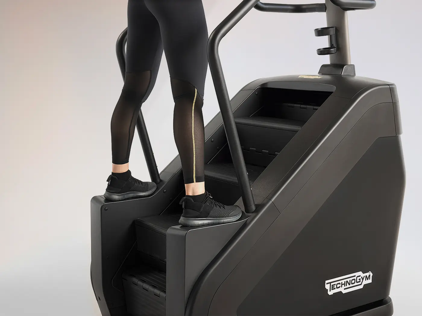 Person standing on the lateral footrests of a stair climber, with both feet positioned on the side platforms beside the moving steps