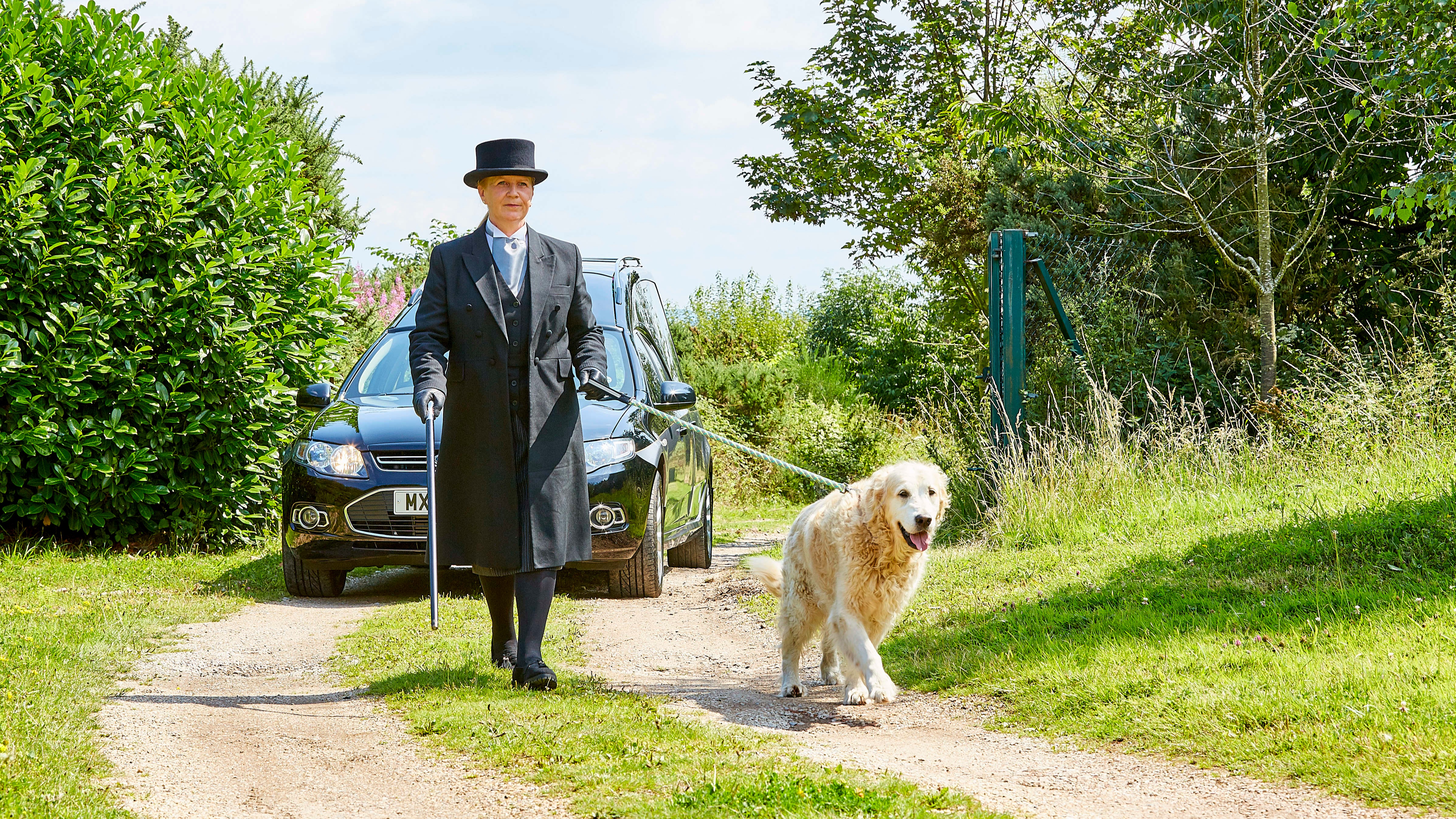 Funeral director at the head of a procession walking a dog. 