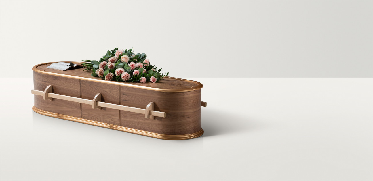 Smooth wooden coffin in dark and light wood with wooden handles and pink rose floral arrangement