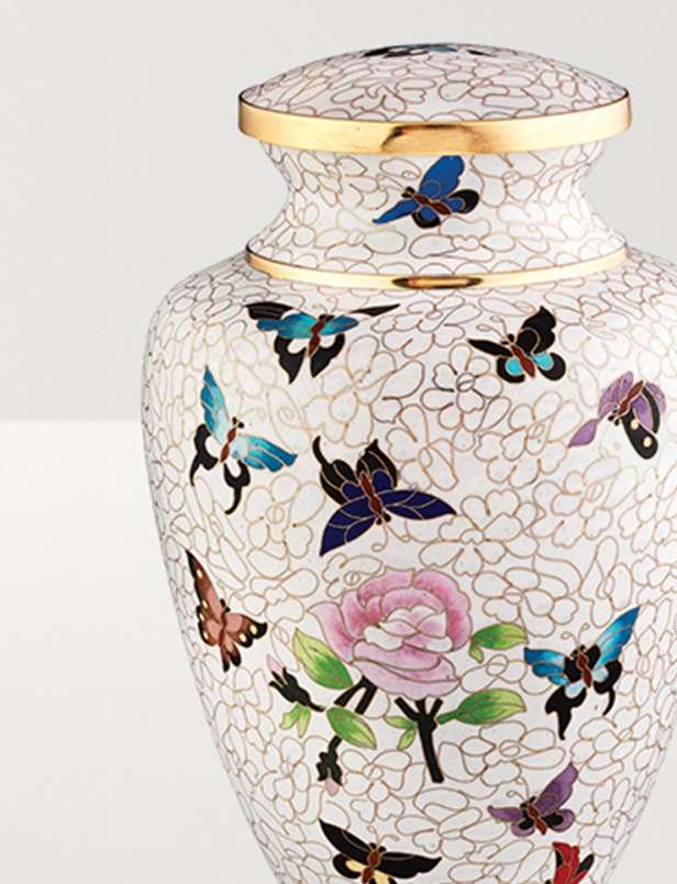 Close up image of a white urn with butterflies and roses and a copper rim
