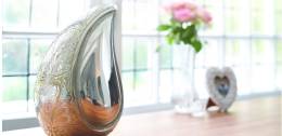 Silver teardrop shaped urn with engraving on one side and a smooth reflection on the other