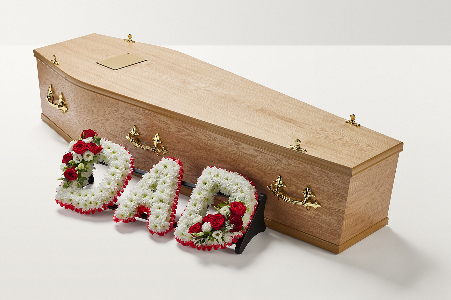 Zoomed out shot of red and white flowers spelling out the word 'Dad' beside coffin