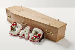 Zoomed out shot of red and white flowers spelling out the word 'Dad' beside coffin