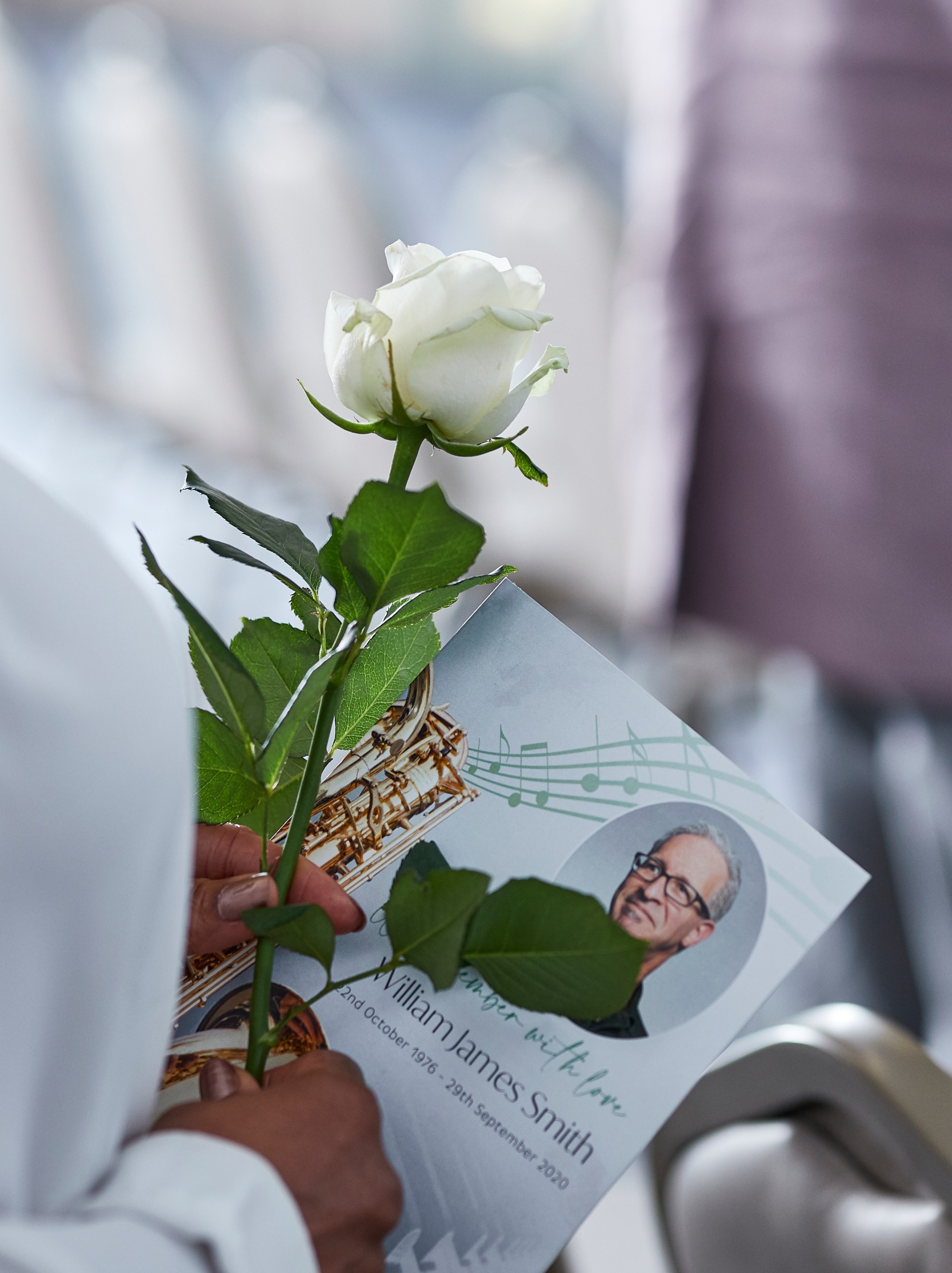 Person holding a single stem rose and an order of service at a funeral