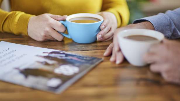 Couple sat at a table with cups of coffee discussing funeral plans.