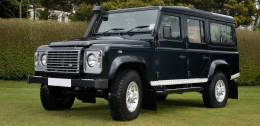 Black Land Rover Hearse parked on grass in front of a hedge
