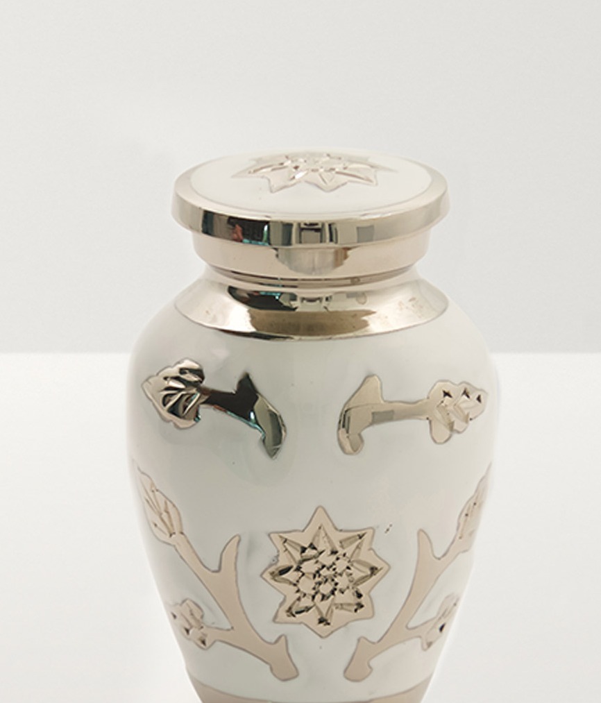 Close up of a white urn with silver floral decoration and rim