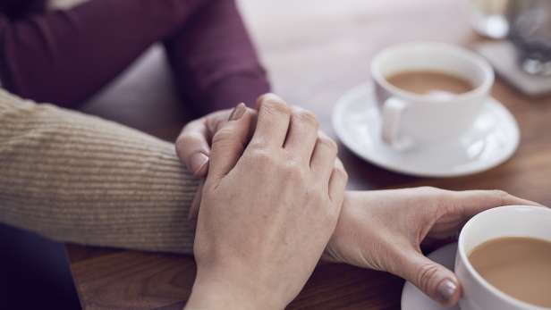 Family members holding hands providing support whilst having a cup of tea. 