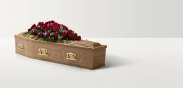 Full length image of a light oak coffin with brass handles and large rose spray