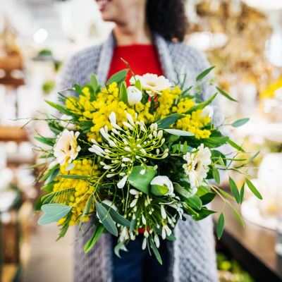 Yellow and white bouquet in a vase in front of a person in a red top and grey cardigan
