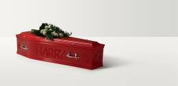 Full length image of a red wooden coffin with 'Harry' engraved on the side and a rose spray