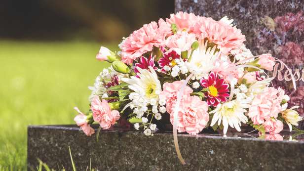 Pink and white flowers laid on a black granite gravestone.