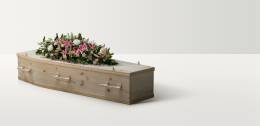 Full length image of a pine coffin with a large bright floral arrangement