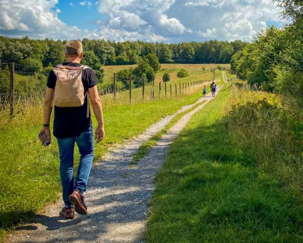 Short haired person with a canvas backpack walking down a country lane 