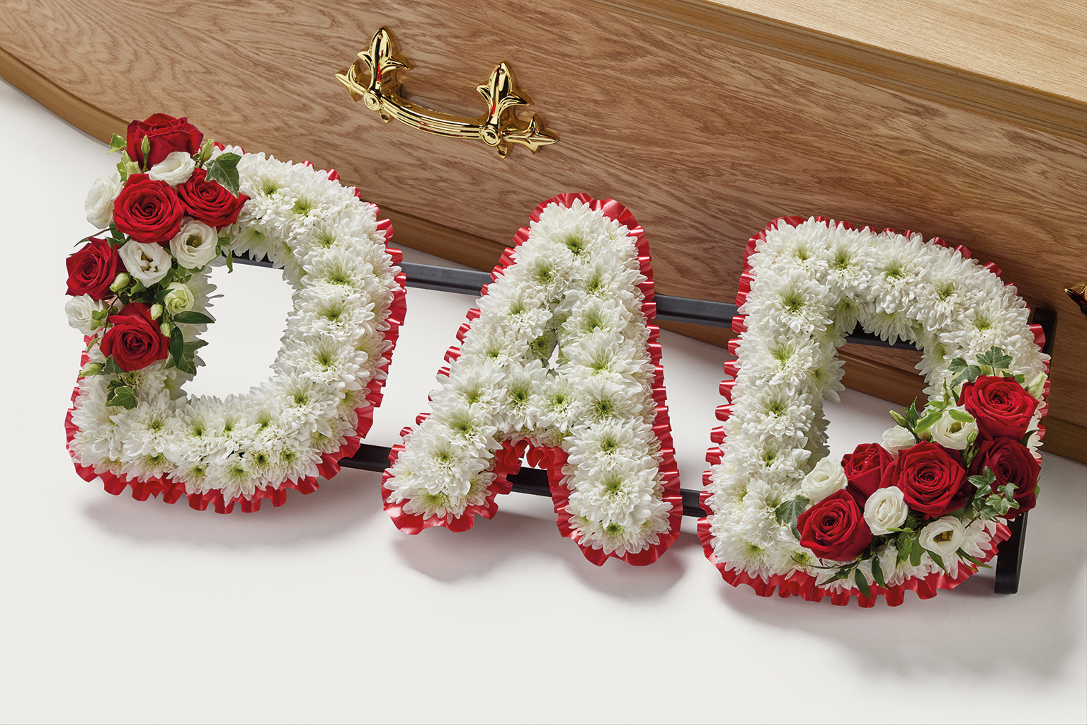White and red flowers spelling out the word 'Dad' beside coffin