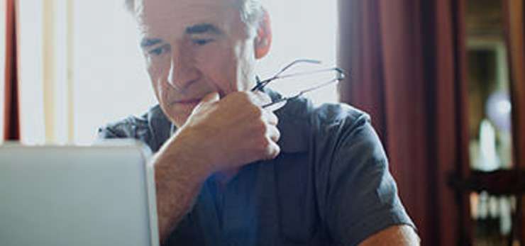 man holding his glasses, using his laptop