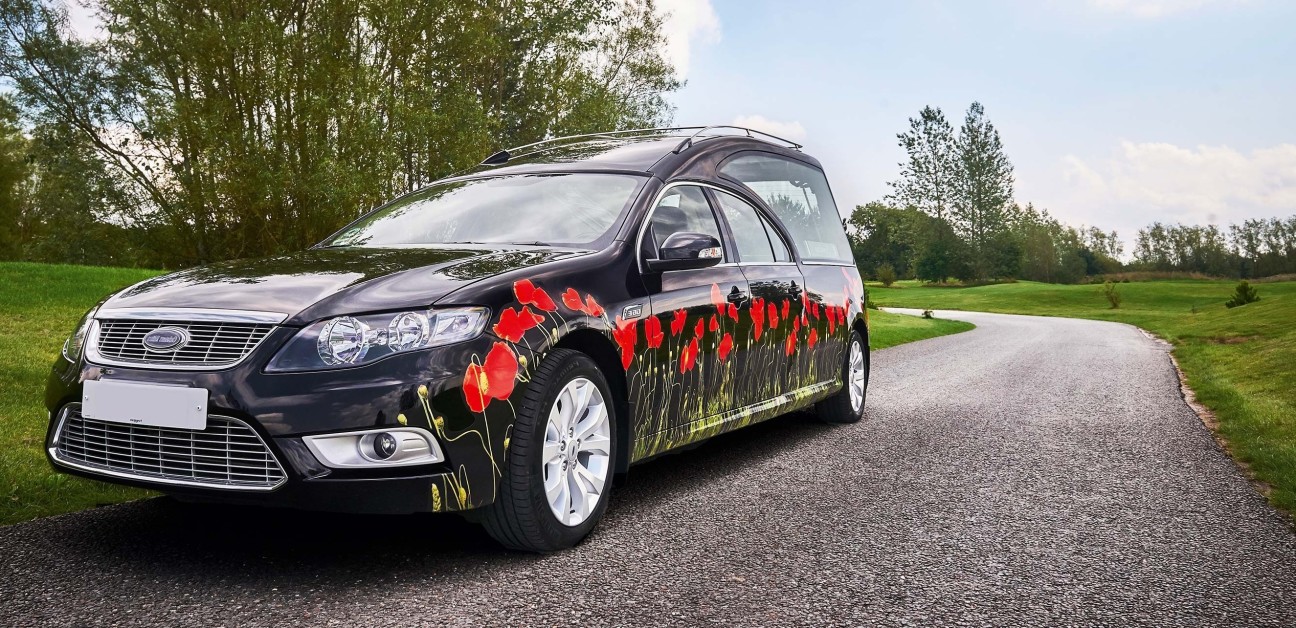 Black hearse with poppies on driving through a green parkland