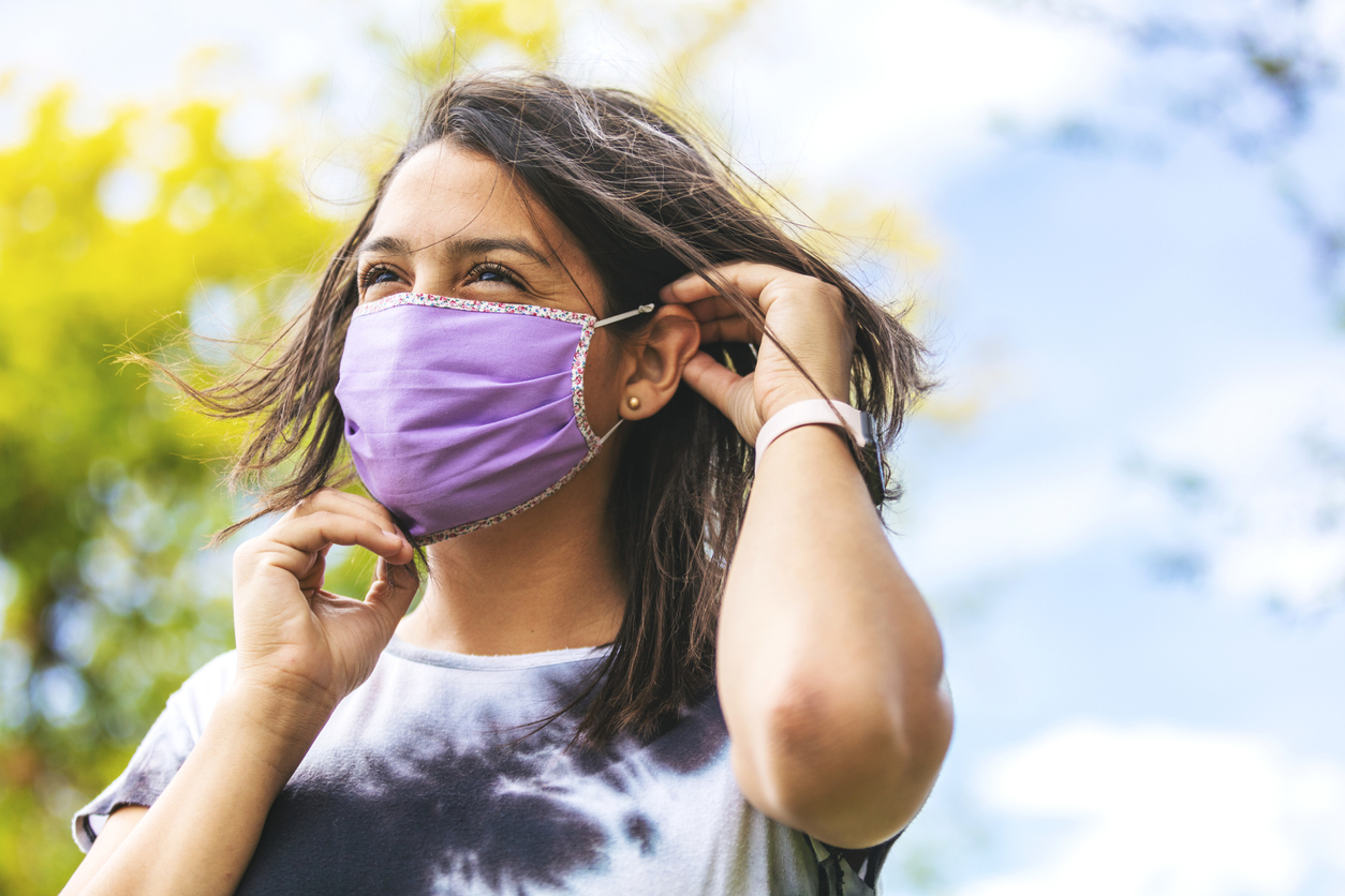 Young woman putting on face mask outdoors