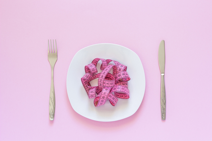 Pink measuring tape lying on a plate with a knife and fork on pink background