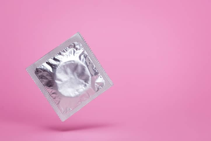 Unopened condom packet on a bright pink background