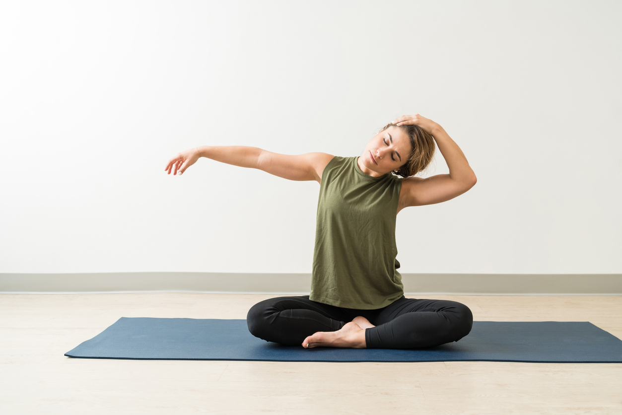 woman sitting on yoga mat stretching neck