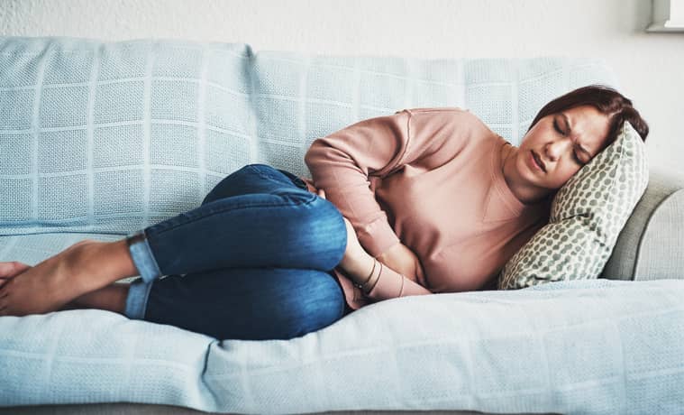 Person with period pain on a sofa holding their tummy