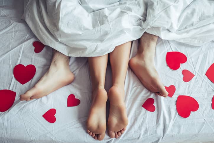 Two pairs of feet sticking out of the bedsheets with paper hearts scattered around