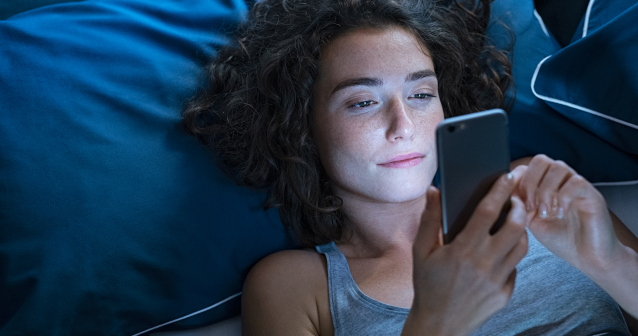 Woman lying awake at night using her phone