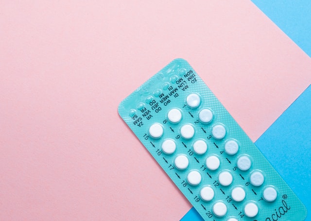 Contraceptive pills in packet on pink and blue background