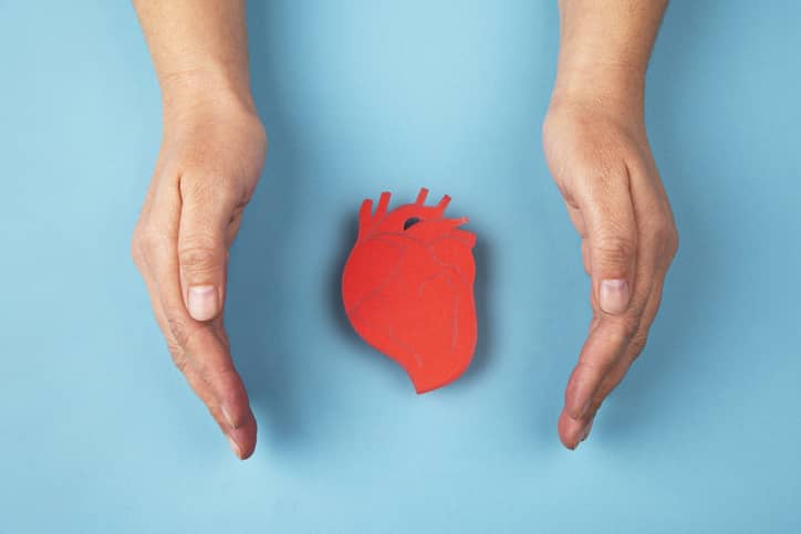 A red paper heart cutout on a blue background with hands either side