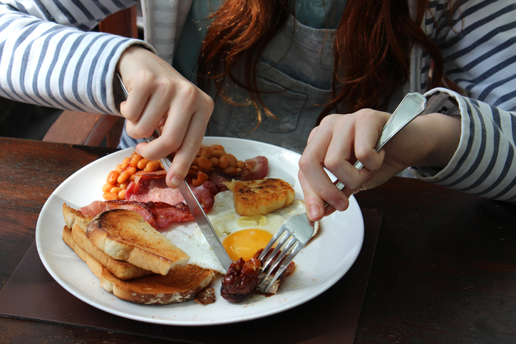 Girl eating a full English fried breakfast at a table