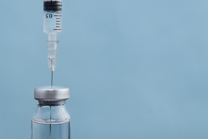 Syringe in bottle of HPV vaccine on blue