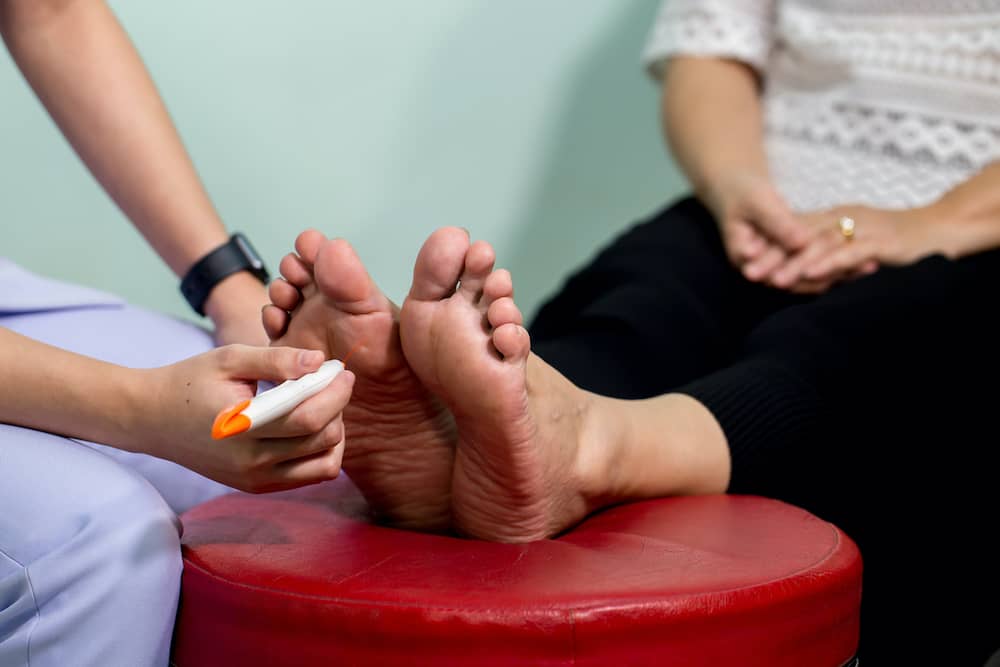 Person with feet on red stool with doctor examining nerves in feet
