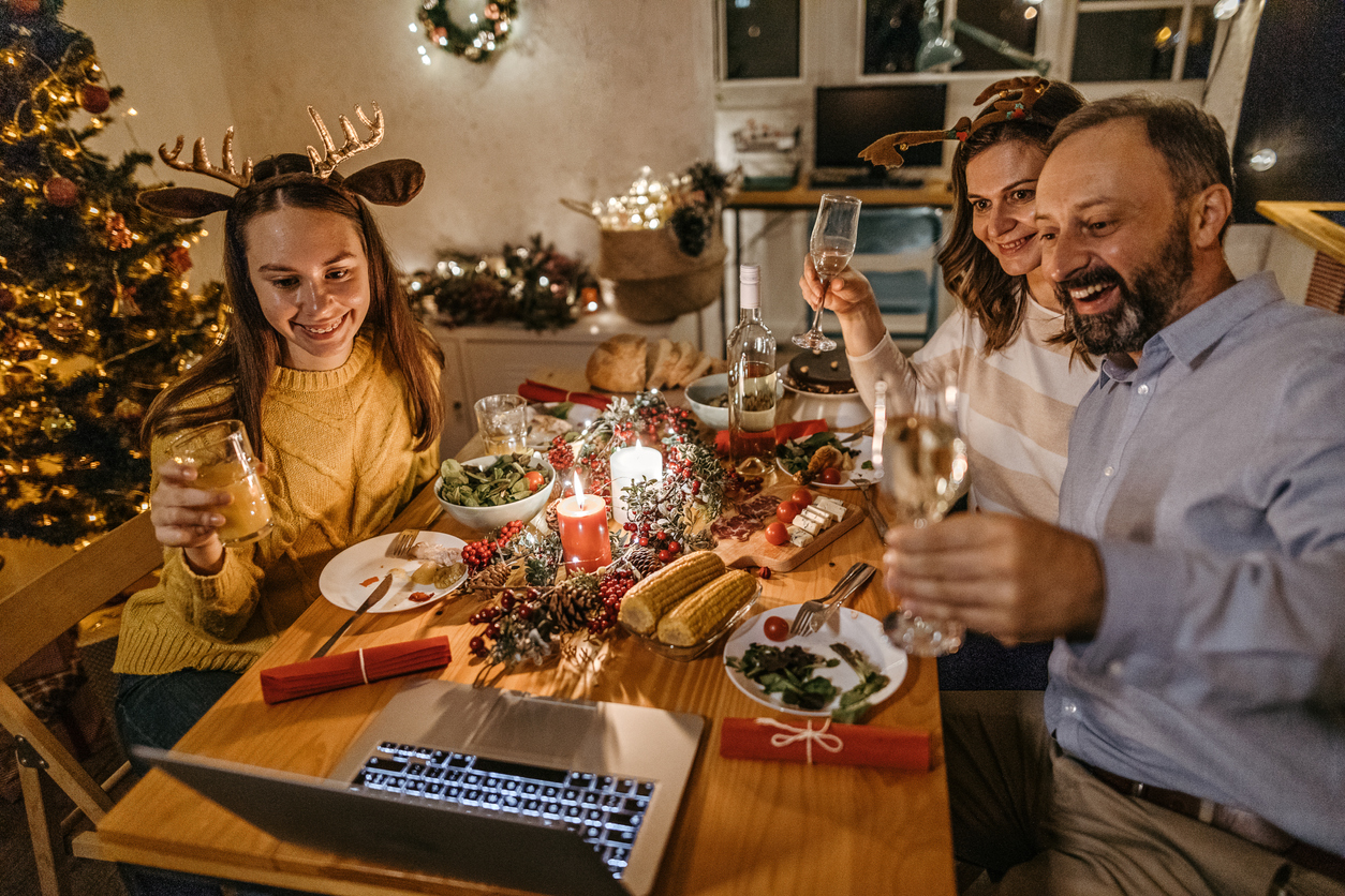 Family toasting drinks on video call using laptop during Christmas dinner celebration (credit - mixetto)