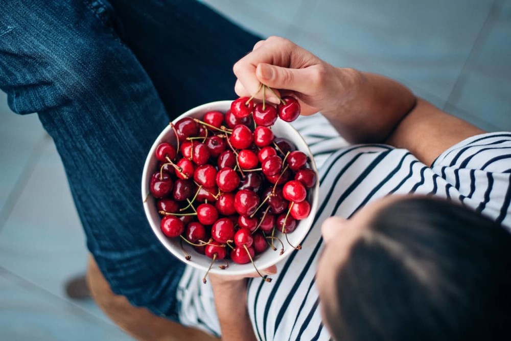 Person in striped T-shirt eating bowl of cherries