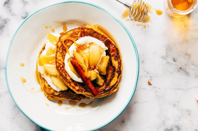 Overhead shot of a plate of stacked pancakes topped with apple slices and drizzled with honey