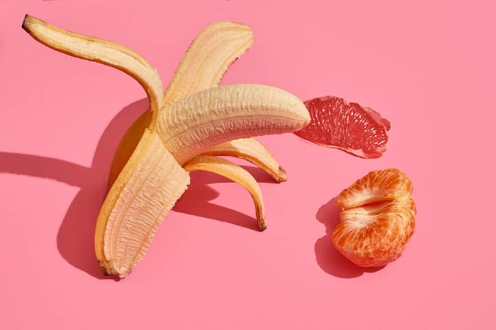 粉红色背景上的未磨损香蕉，橙色和葡萄柚
