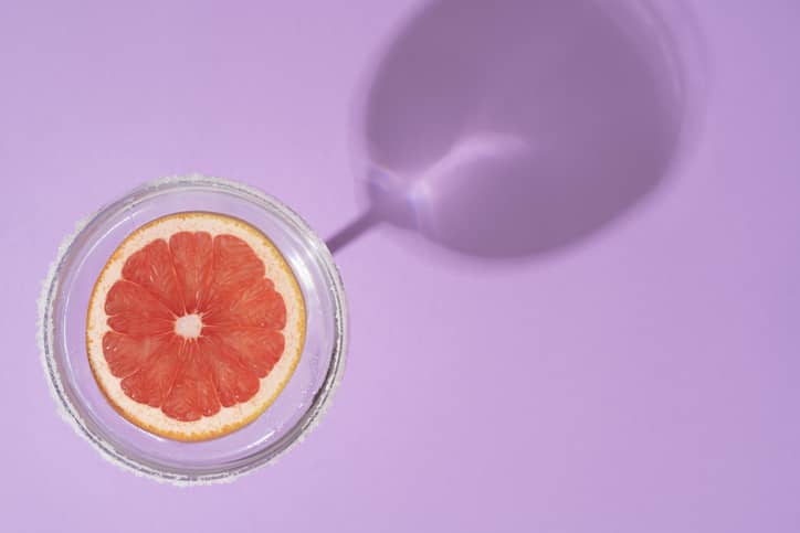 Grapefruit slice in cocktail glass on soft pastel purple background