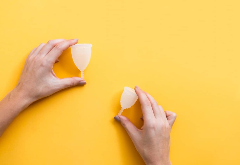 Hands holding 2 sizes of menstrual cups on yellow background