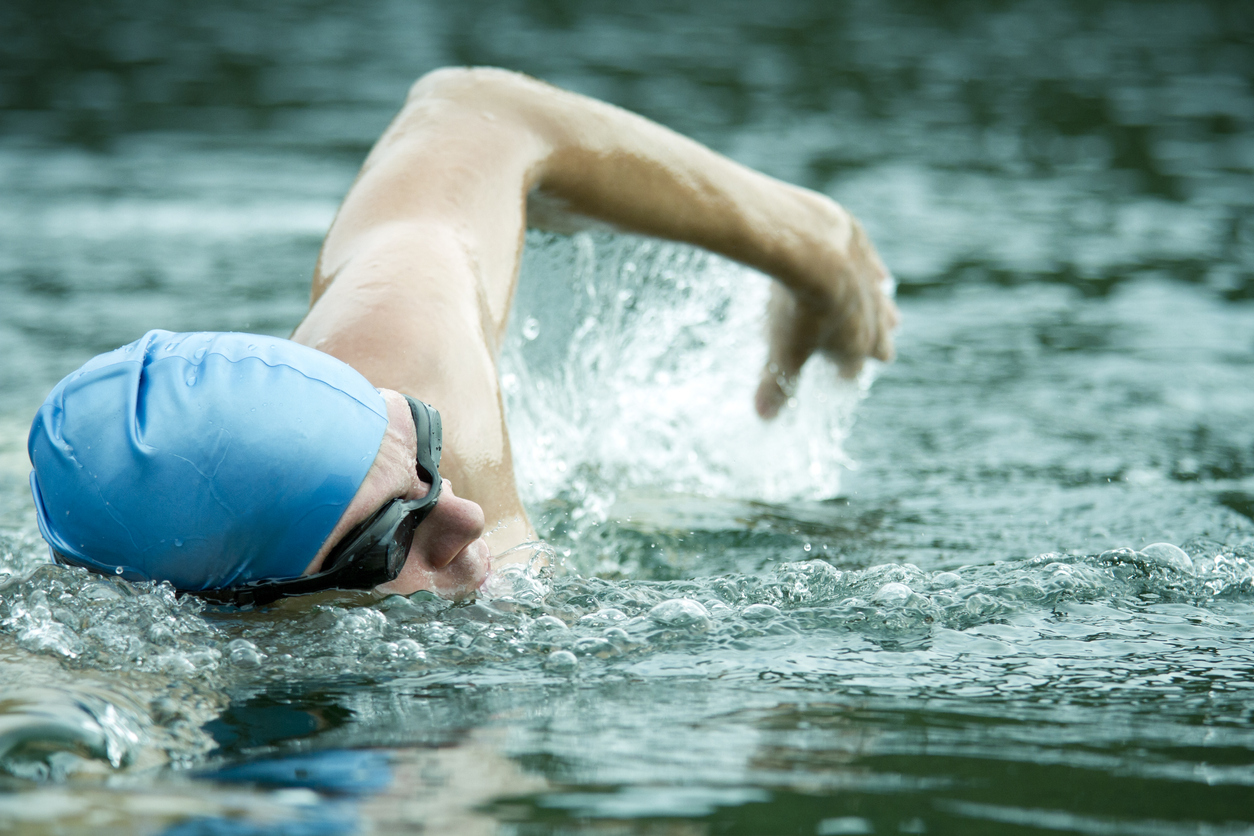 Man swimming in water, wearing goggles and swimming hat