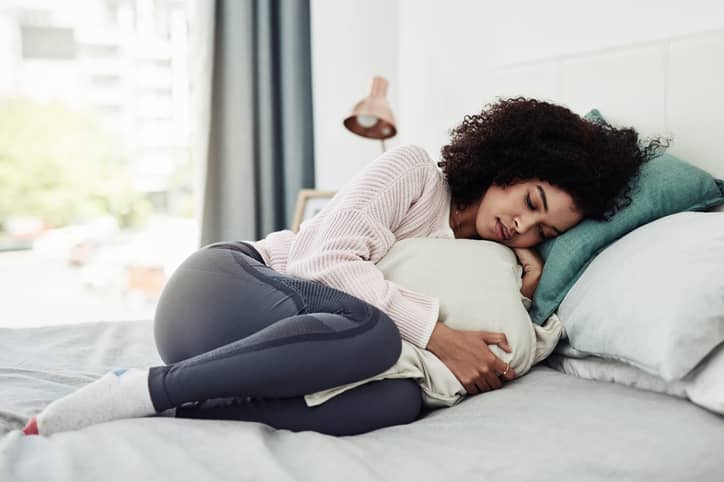 Person lying on bed curled up and holding a pillow