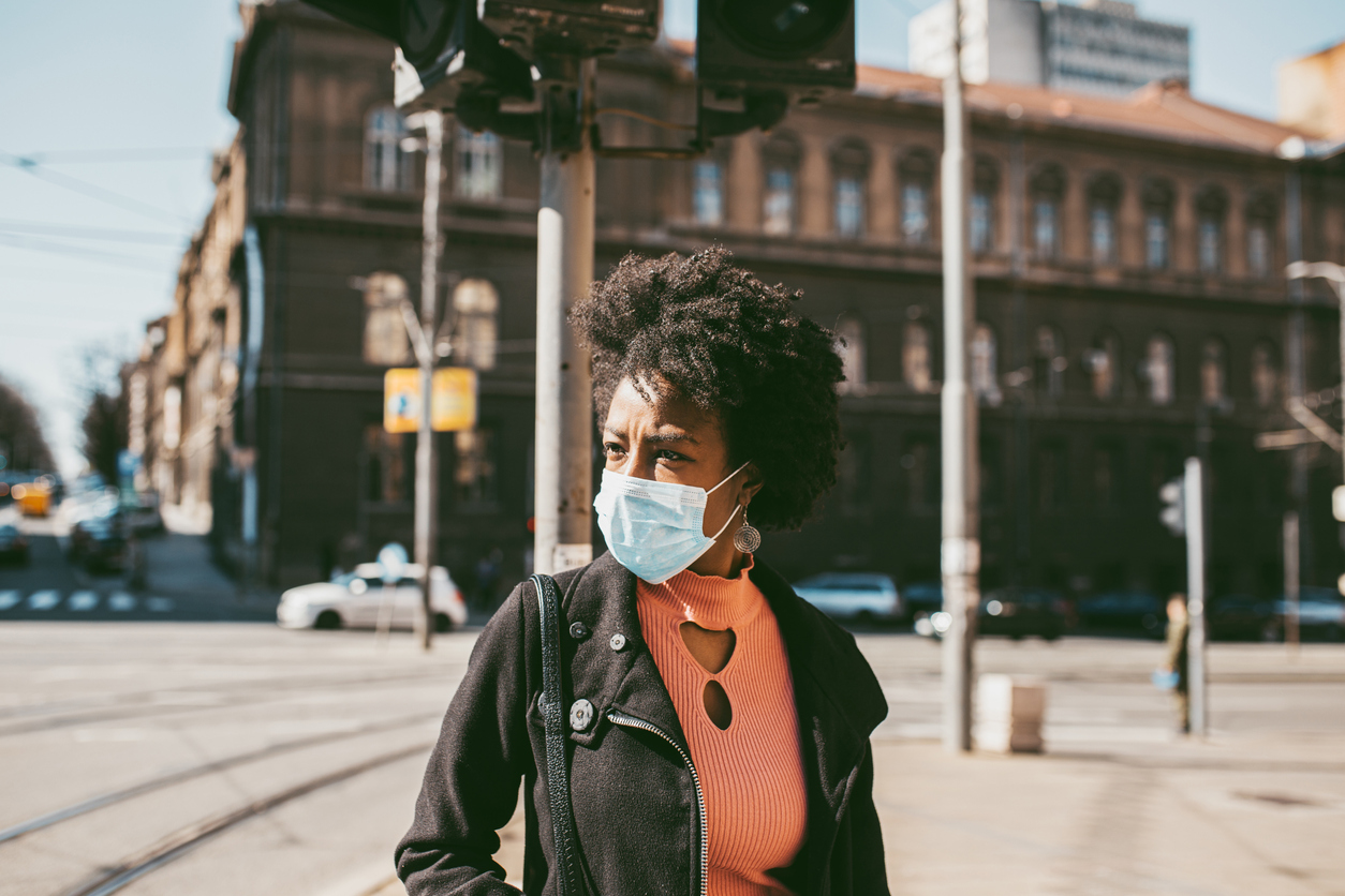黑人妇女戴着手术面具站在城市的户外