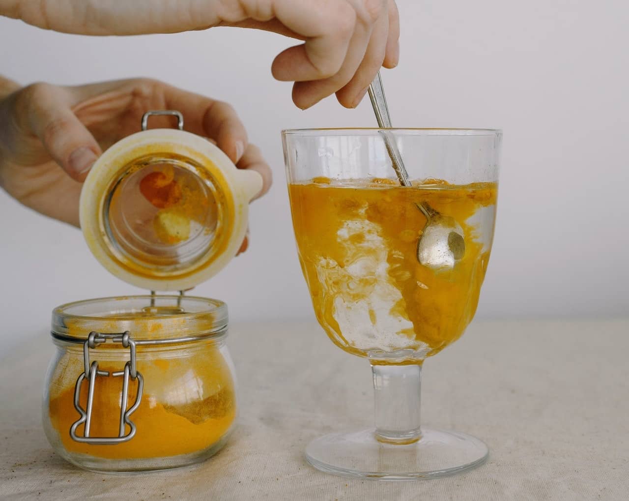 Crop hands adding turmeric in glass of hot water in morning