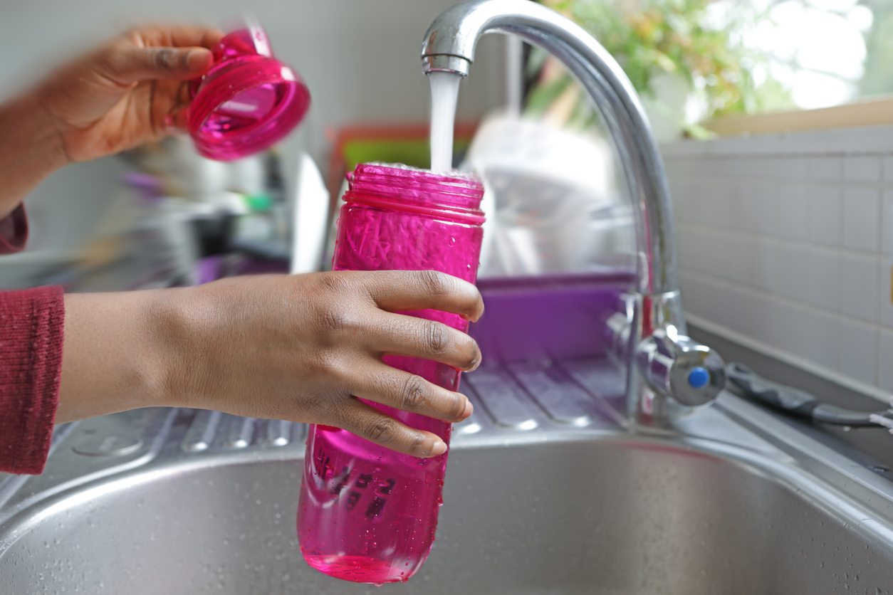 Running tap, water running into a pink water bottle held over a sink